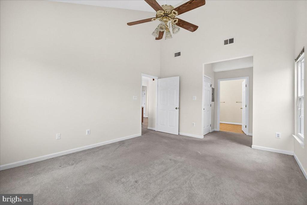 Empty carpeted room with a ceiling fan, window, and two open doorways.