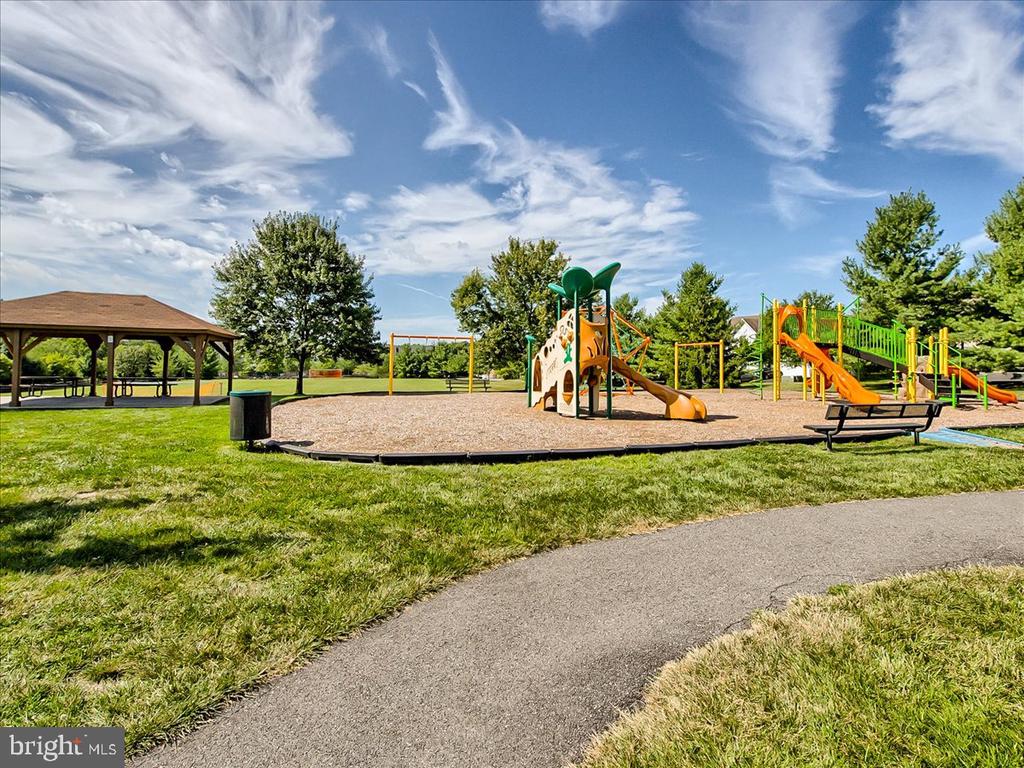 Community playground with colorful play structures, a pavilion, and paved walking path.