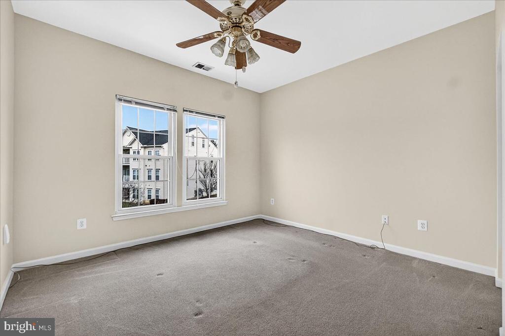 Empty bedroom with gray carpet, two windows, and a wooden ceiling fan.