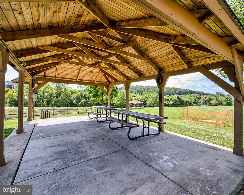 Picnic pavilion with wooden roof and tables beside a grassy recreation field.