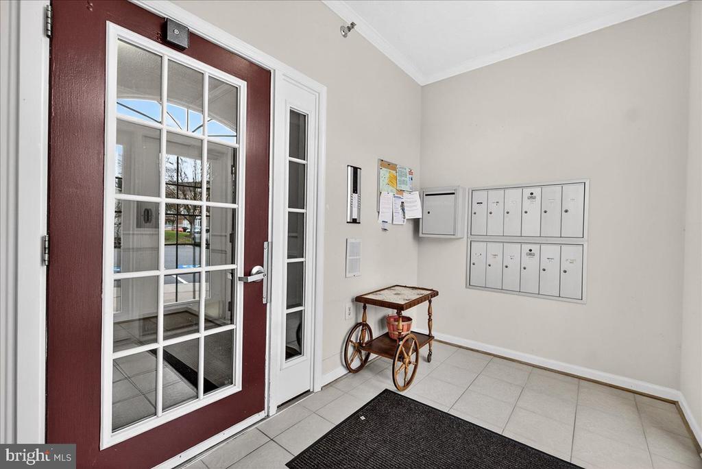 Lobby entry with wall-mounted mailboxes, a burgundy glass-paneled door, and tiled floor.