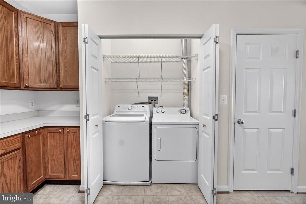Laundry area with washer and dryer in an open closet beside wood cabinets and a countertop.