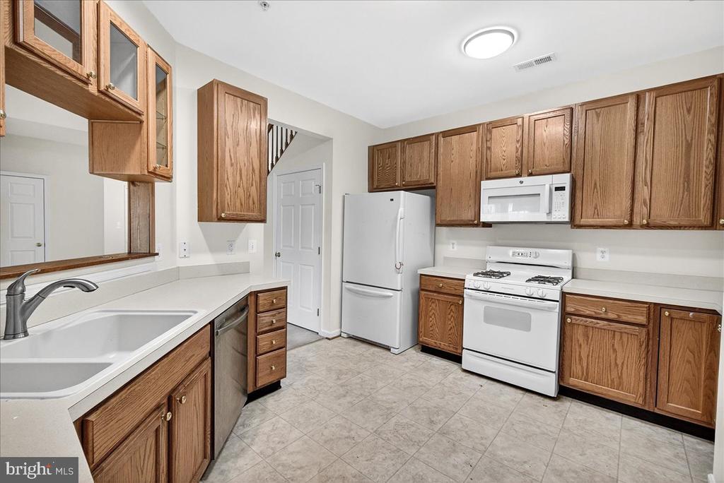 Kitchen with oak cabinets, white countertops, a double-basin sink, and white appliances.