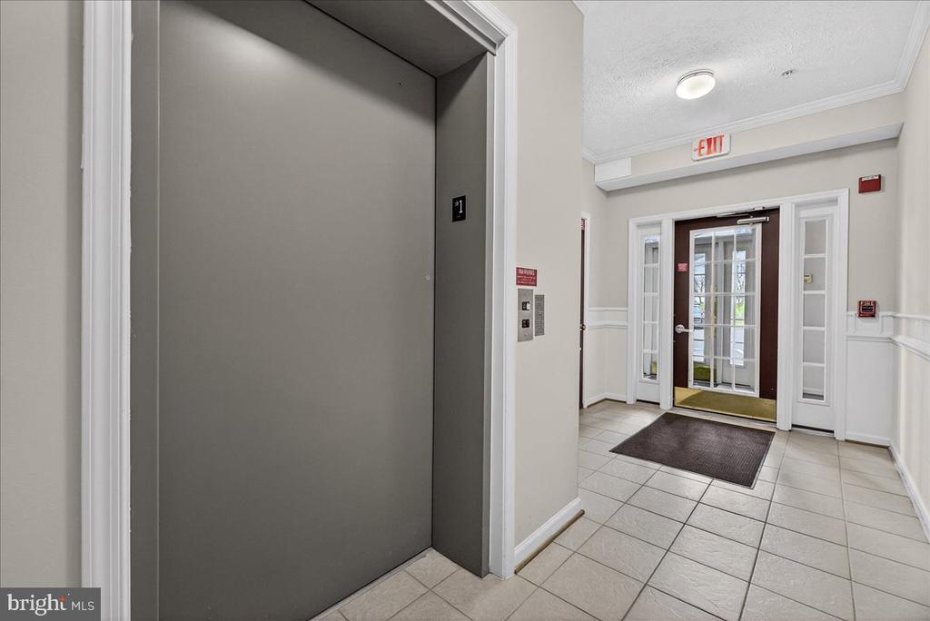 Elevator opening onto a tiled building lobby with glass-paneled entrance doors.