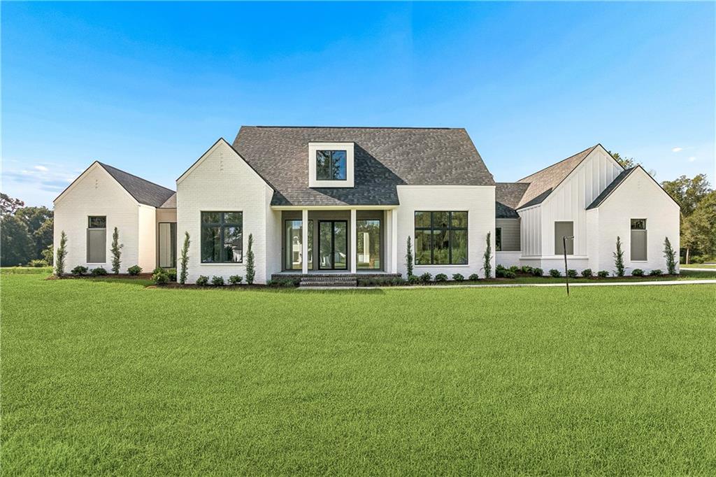 White modern farmhouse with dark roofs, black-framed windows, and a broad green lawn.