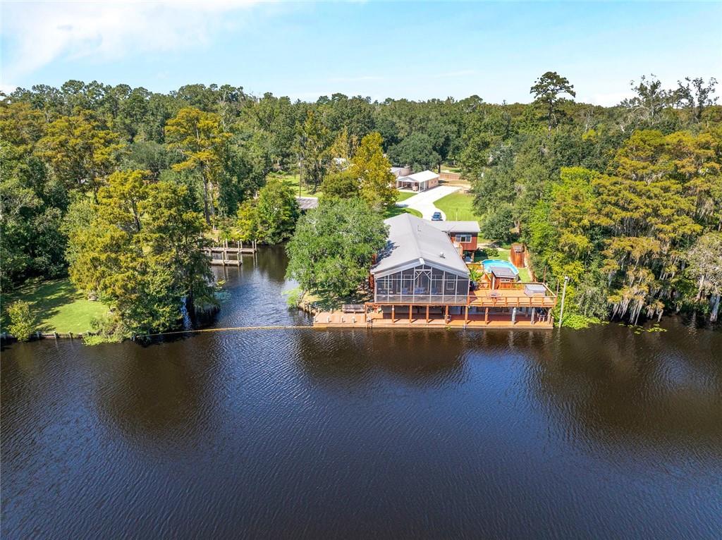 Waterfront home with a screened porch, broad deck, and small pool beside a tree-lined waterway.