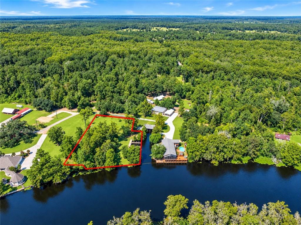 Aerial view of a wooded waterfront parcel outlined in red beside a river.