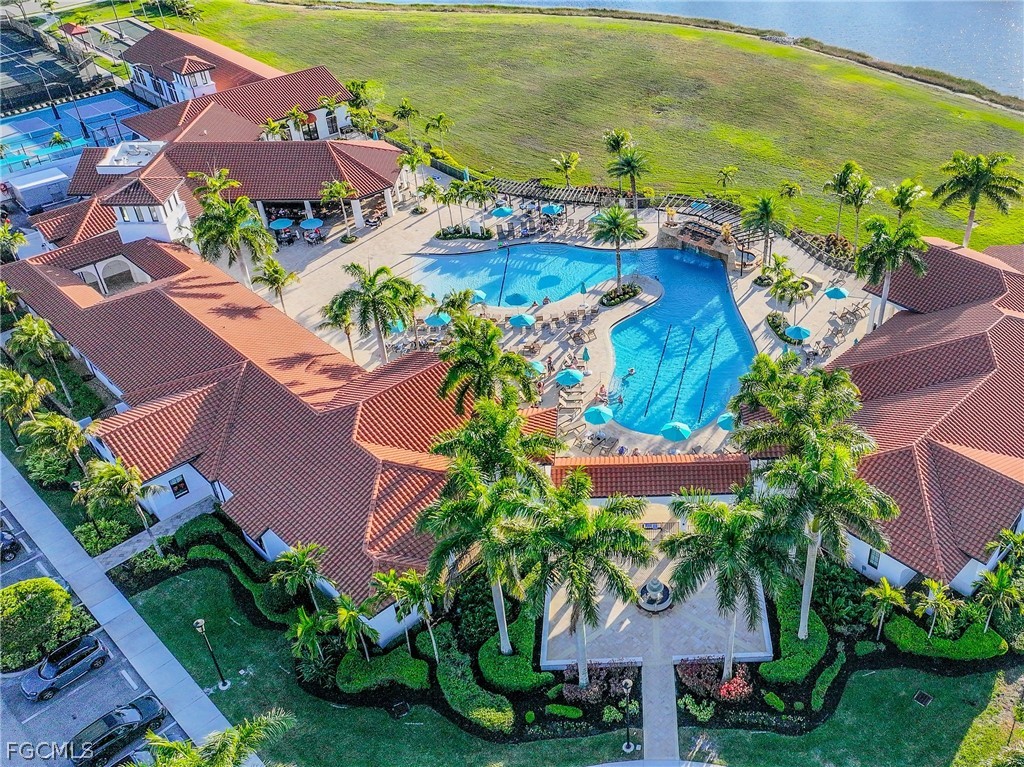 Aerial view of a community pool surrounded by red-tile-roof buildings and palm trees.