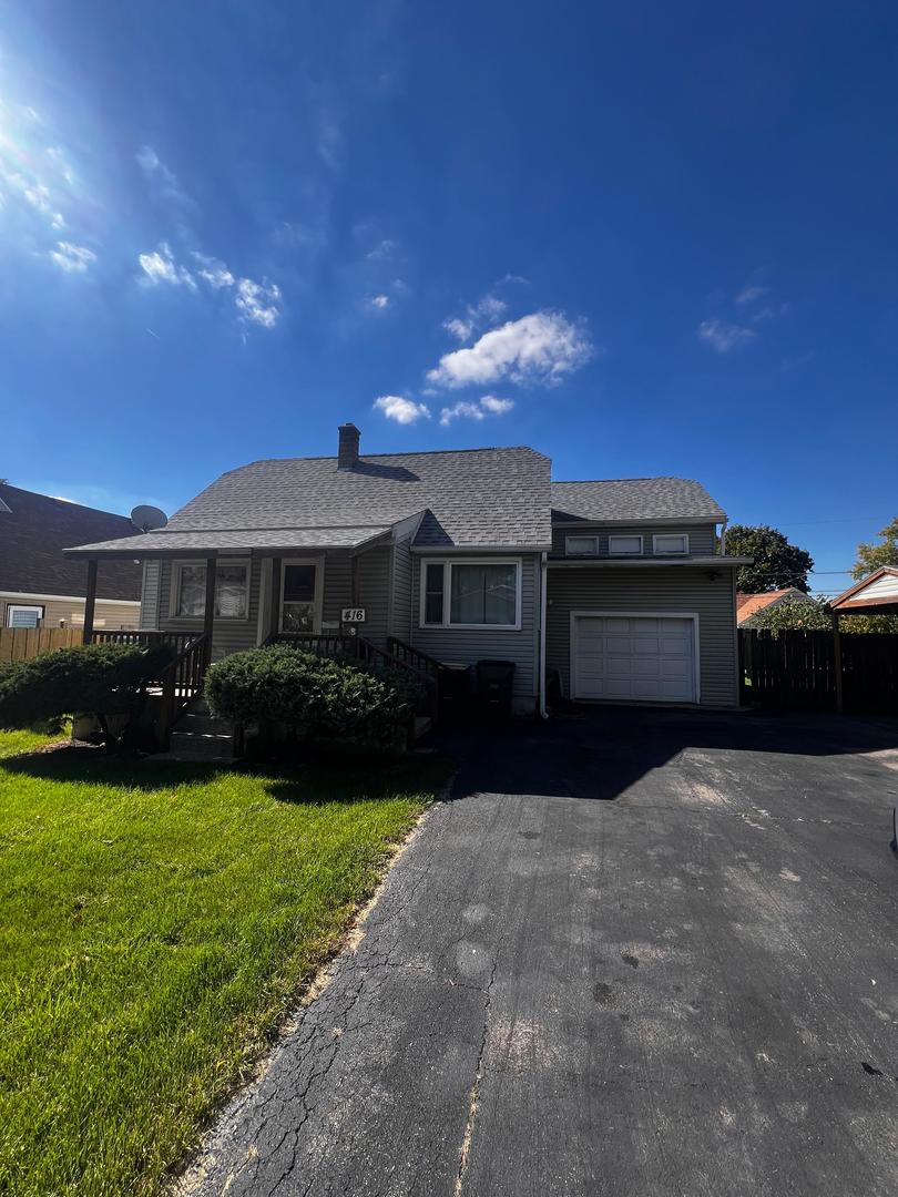 Gray house with a covered porch, attached garage, lawn, and paved driveway.
