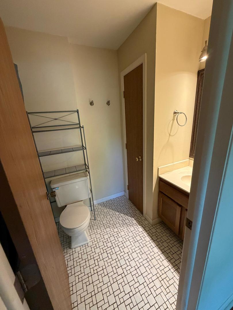 Bathroom with a wood vanity, white sink, toilet, metal shelving, and geometric-pattern tile floor.