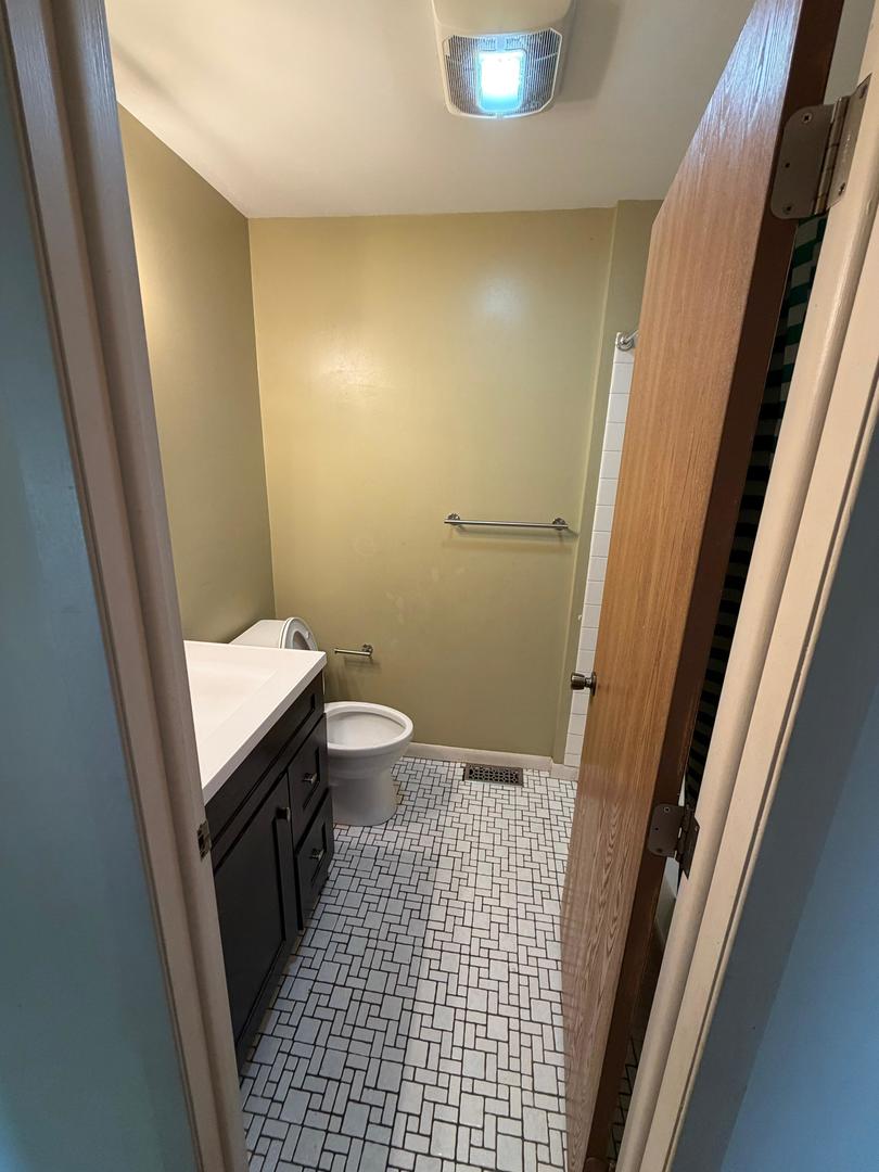 Bathroom with a dark vanity, toilet, and white geometric tile floor.