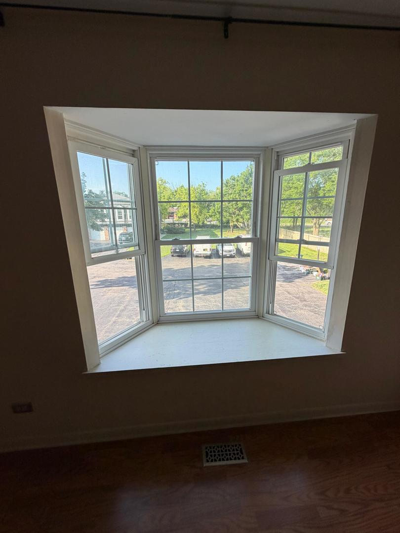 Bay window with a wide sill overlooking a parking area and leafy trees.