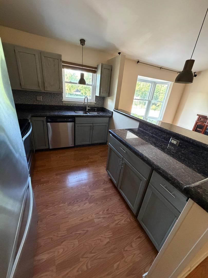 Kitchen with gray cabinetry, dark granite counters, a large island, stainless appliances, and hardwood floors.