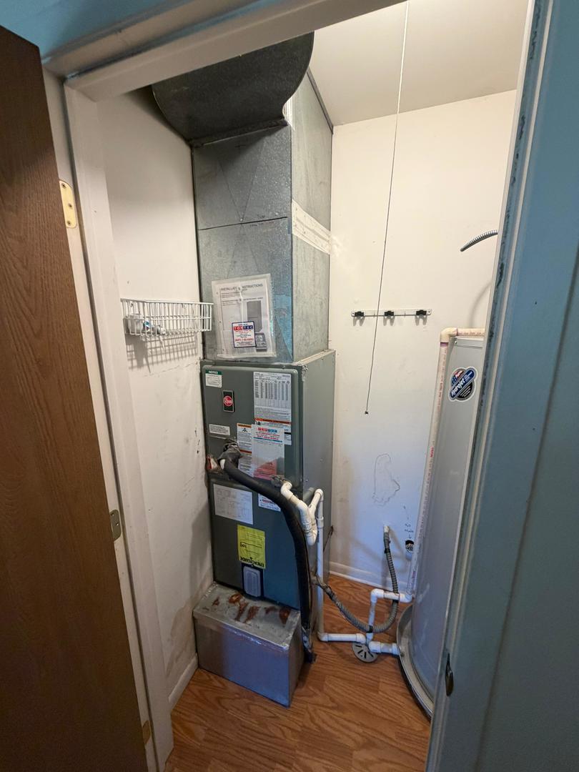 Utility closet with an HVAC furnace, exposed plumbing, and a curved shower enclosure.