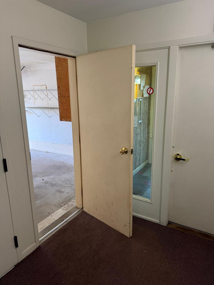 Vacant carpeted interior with an open doorway to a bare storage room and a glass-panel door.