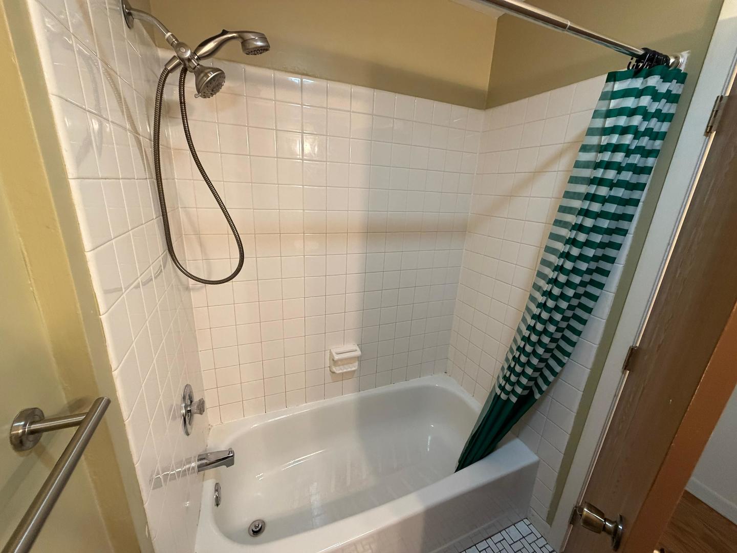 Bathroom with a white tiled tub and shower and a green-and-white striped curtain.