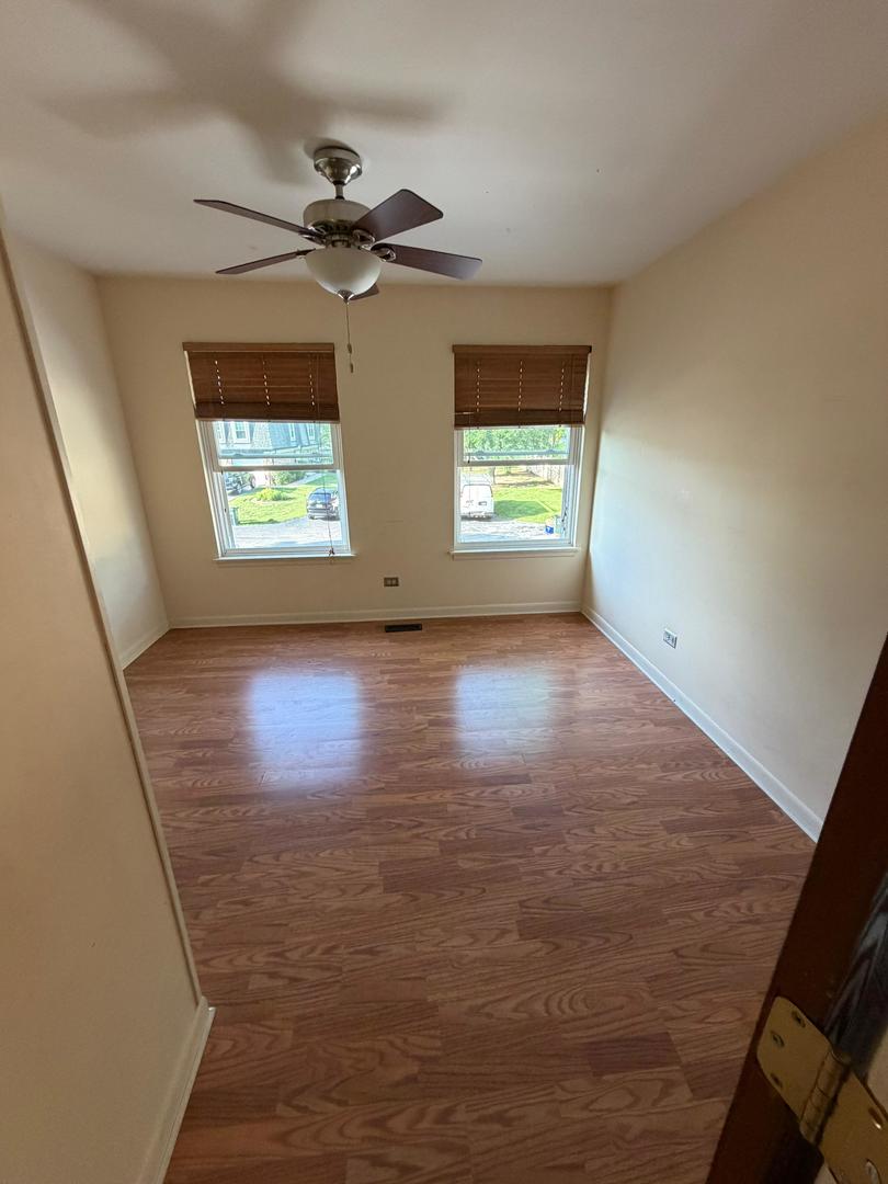 Empty bedroom with wood-look floors, a ceiling fan, and two windows with blinds.