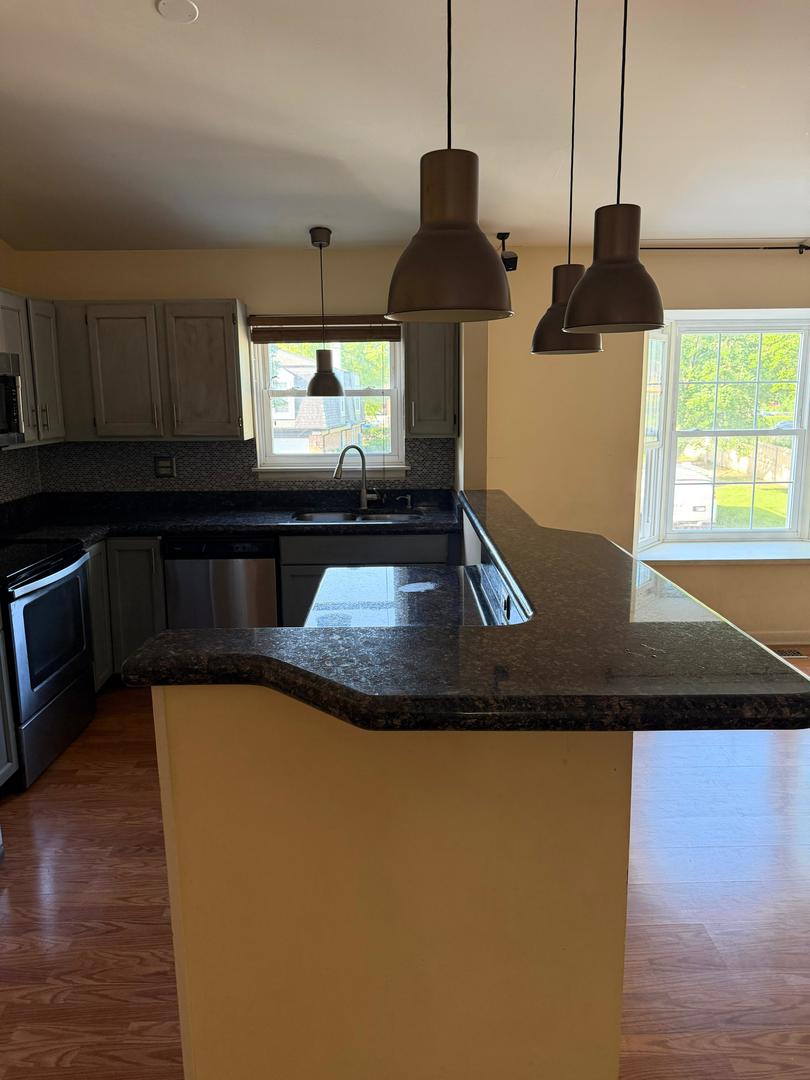 Kitchen with a granite peninsula, gray cabinets, stainless steel appliances, and windows overlooking a yard.