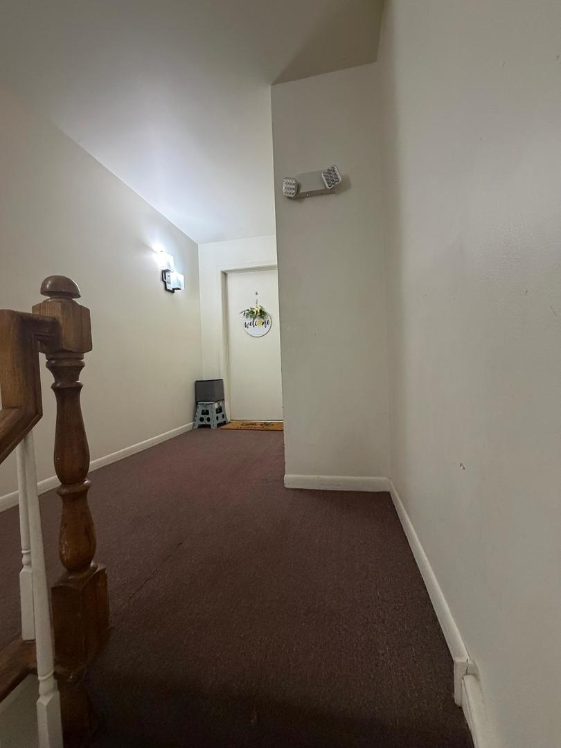 Carpeted hallway with a wooden stair railing and a door bearing a welcome sign.