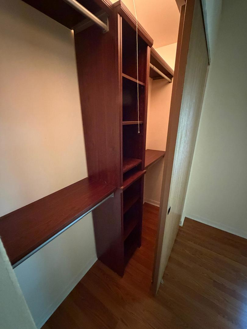 Walk-in closet with dark wood built-in shelves, hanging rods, and hardwood flooring.