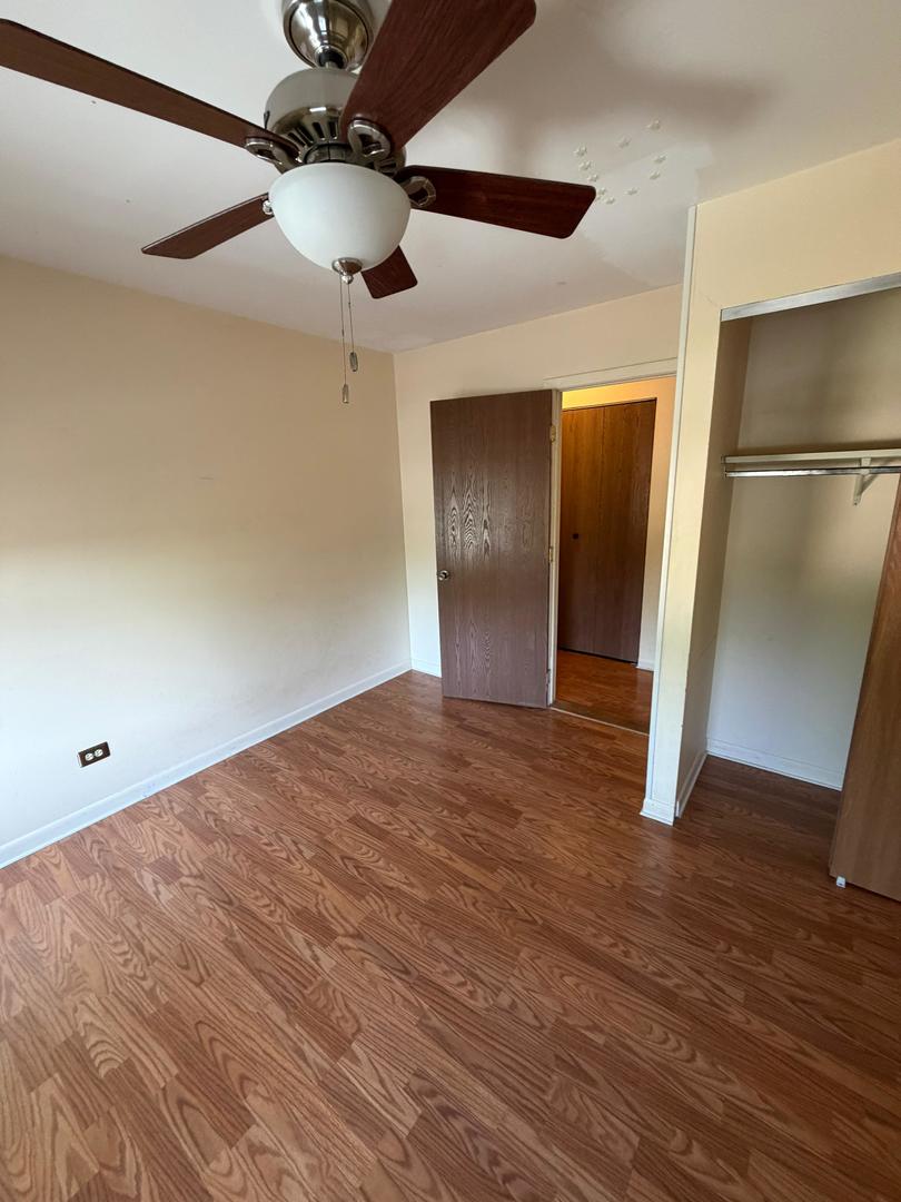 Empty bedroom with wood-pattern flooring, a ceiling fan, and an open closet.