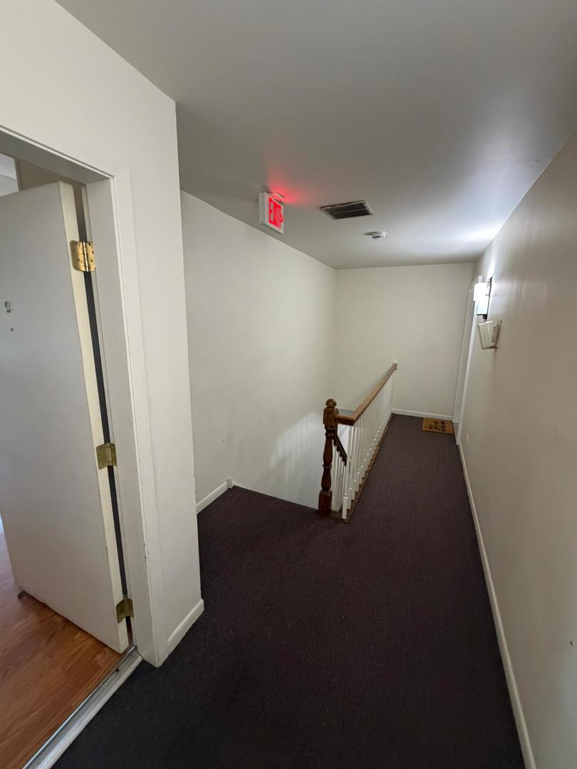 Carpeted hallway beside an open doorway and stair railing.