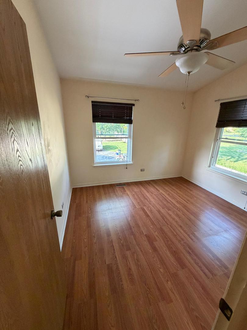Empty bedroom with wood-look floors, two windows with dark blinds, and a ceiling fan.