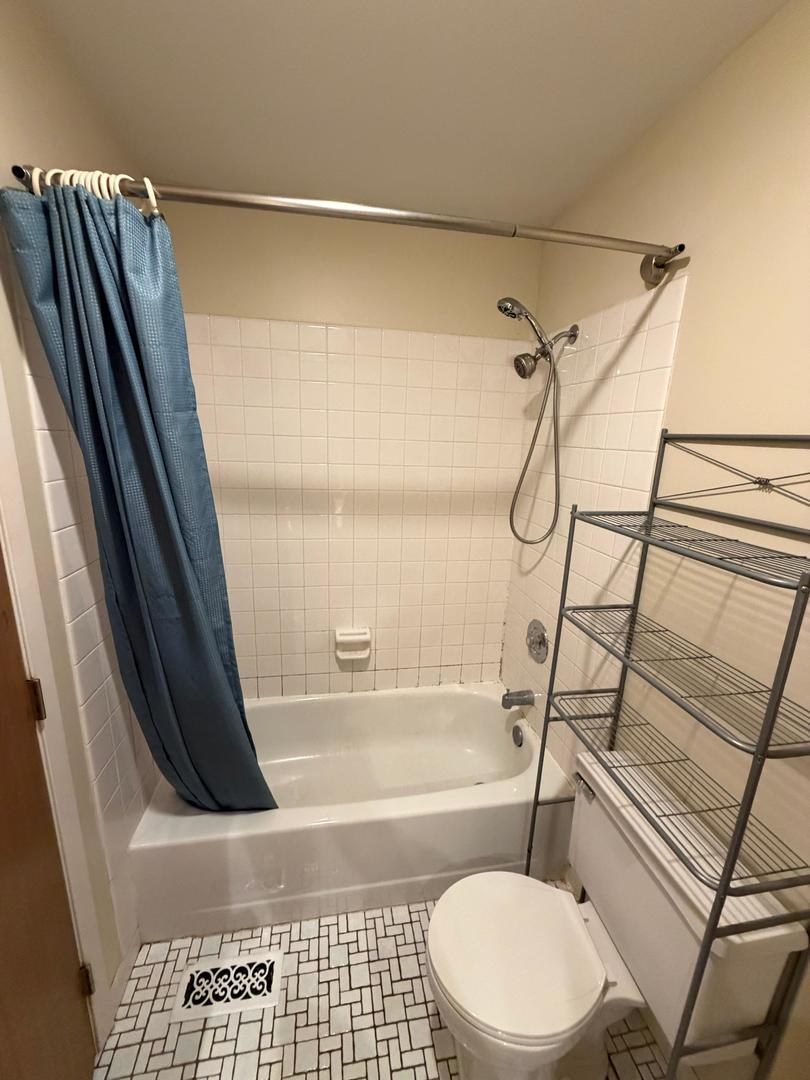 Bathroom with a white tub, blue shower curtain, toilet, and metal storage rack.