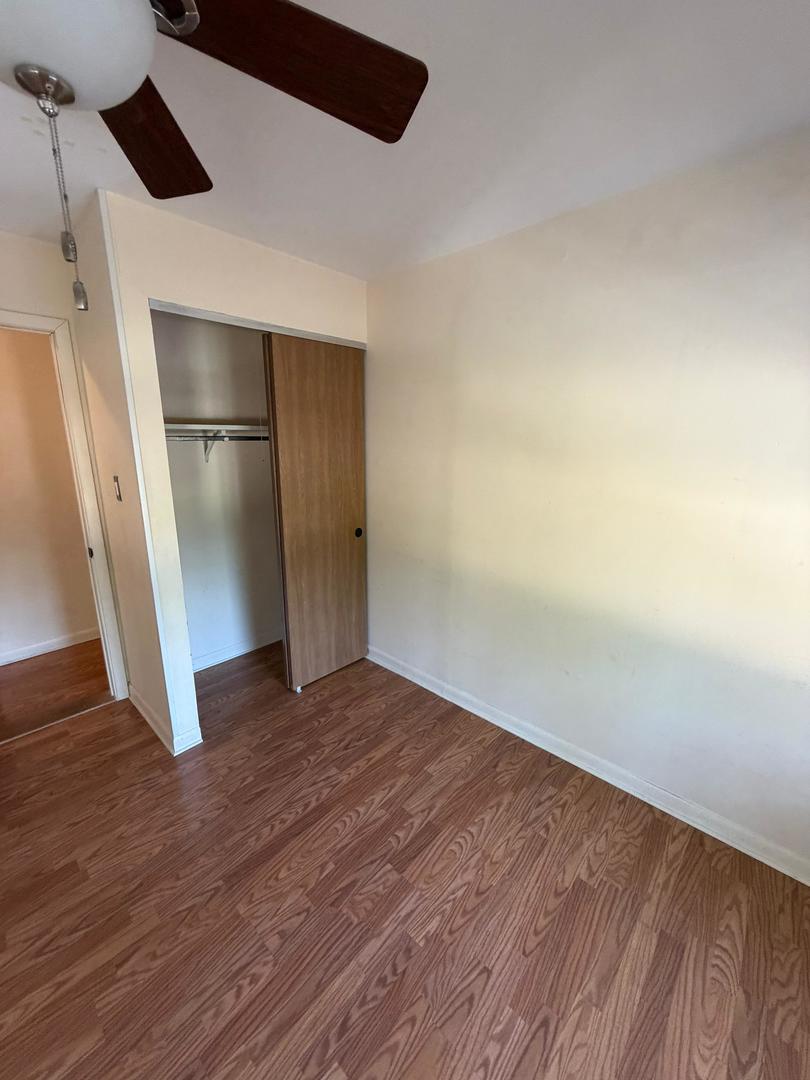 Unfurnished bedroom with wood-look floors, an open closet, and a ceiling fan.