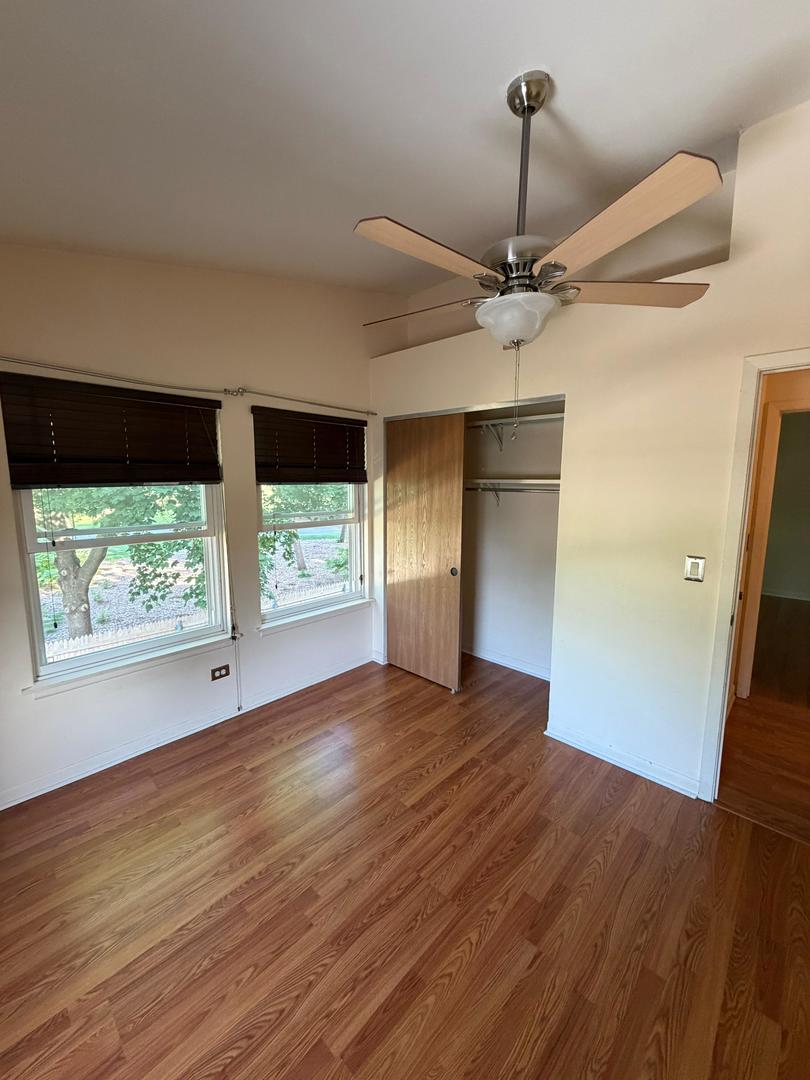 Empty bedroom with wood-look flooring, two shaded windows, an open closet, and a ceiling fan.
