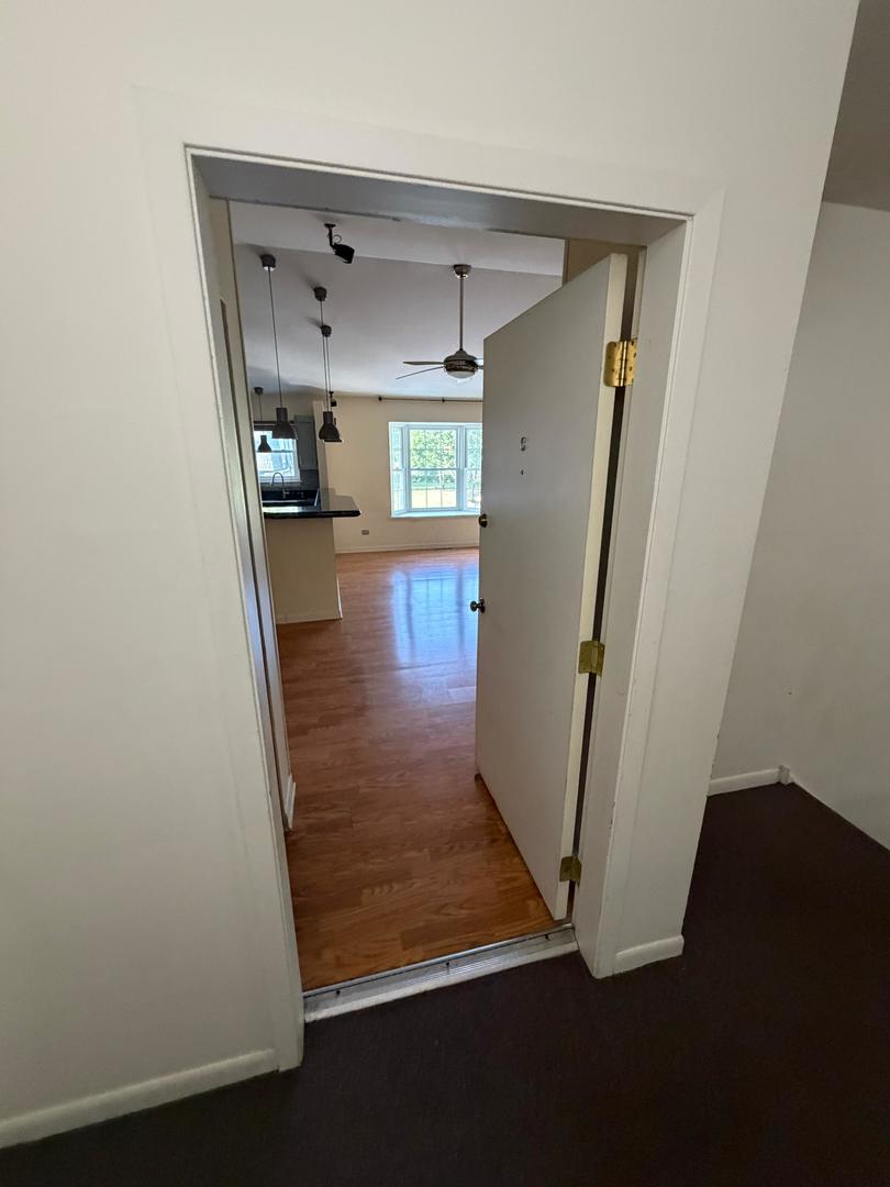 Unfurnished living area with hardwood floors, a ceiling fan, and a bright window beyond the doorway.