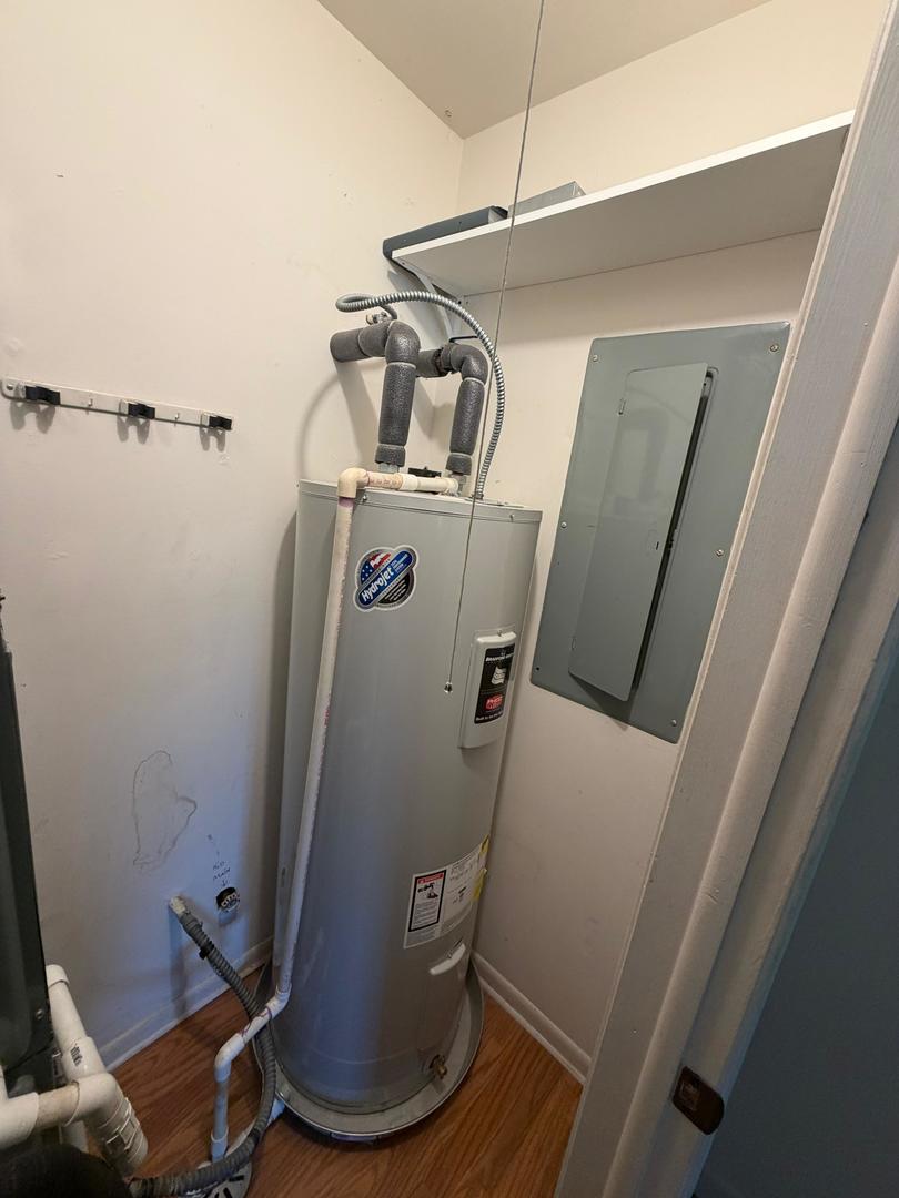 Utility closet with a gray water heater, exposed pipes, and an electrical panel.