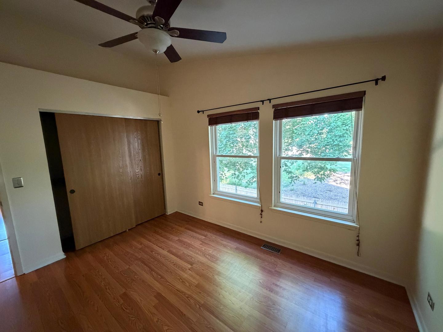 Empty bedroom with hardwood floors, a ceiling fan, sliding-door closet, and two windows.