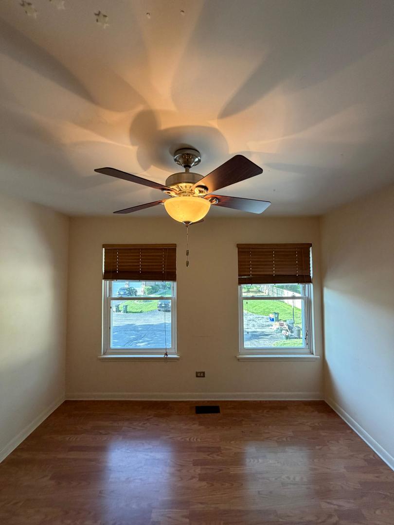 Empty room with wood floors, two windows with blinds, and a ceiling fan.