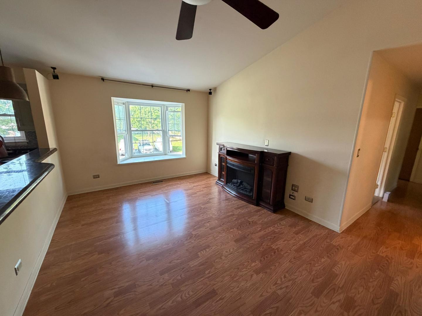 Empty living room with hardwood floors, a bay window, and a dark fireplace surround.