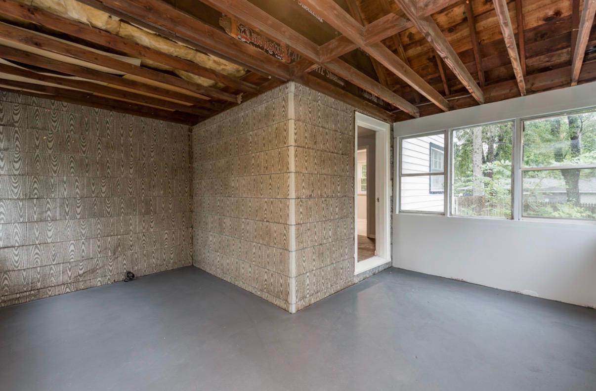 Empty enclosed room with patterned walls, exposed wooden ceiling framing, and large windows.