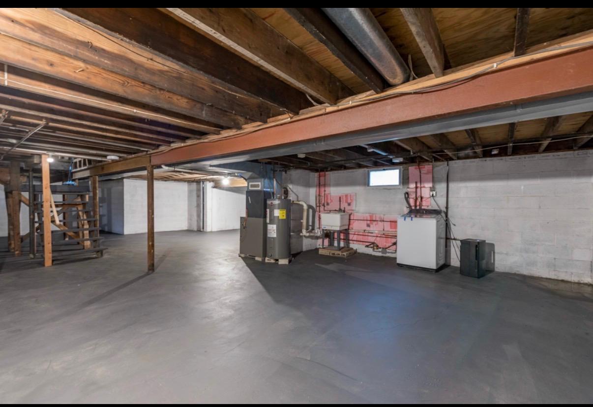 Unfinished basement with a concrete floor, exposed ceiling joists, support beams, and utility equipment.