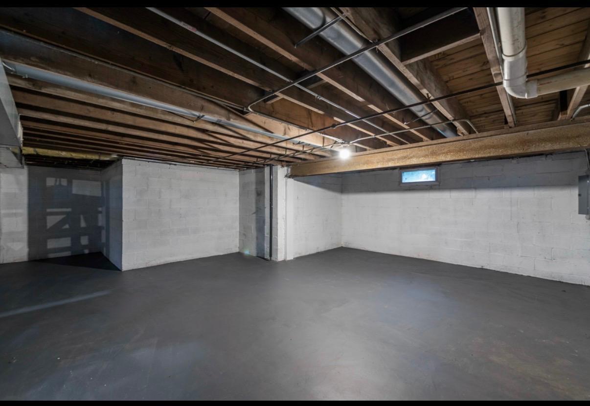 Empty basement with a concrete floor, block walls, exposed ceiling joists, and overhead ductwork.