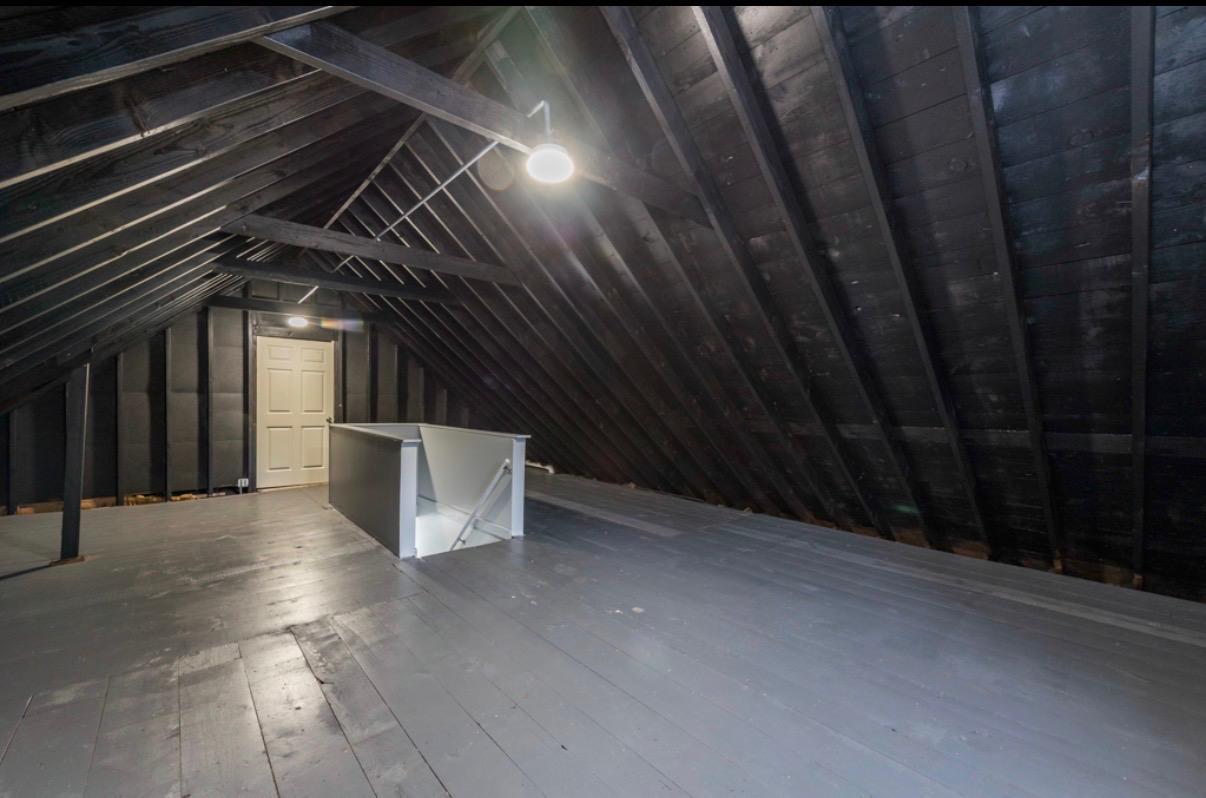 Unfinished attic with exposed rafters, gray plank flooring, and a white access hatch.