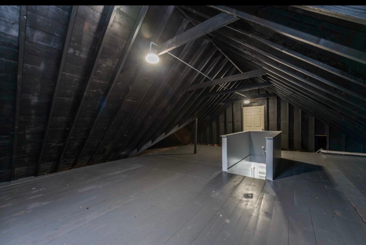 Unfinished attic with exposed rafters, plank flooring, and an open stairwell.