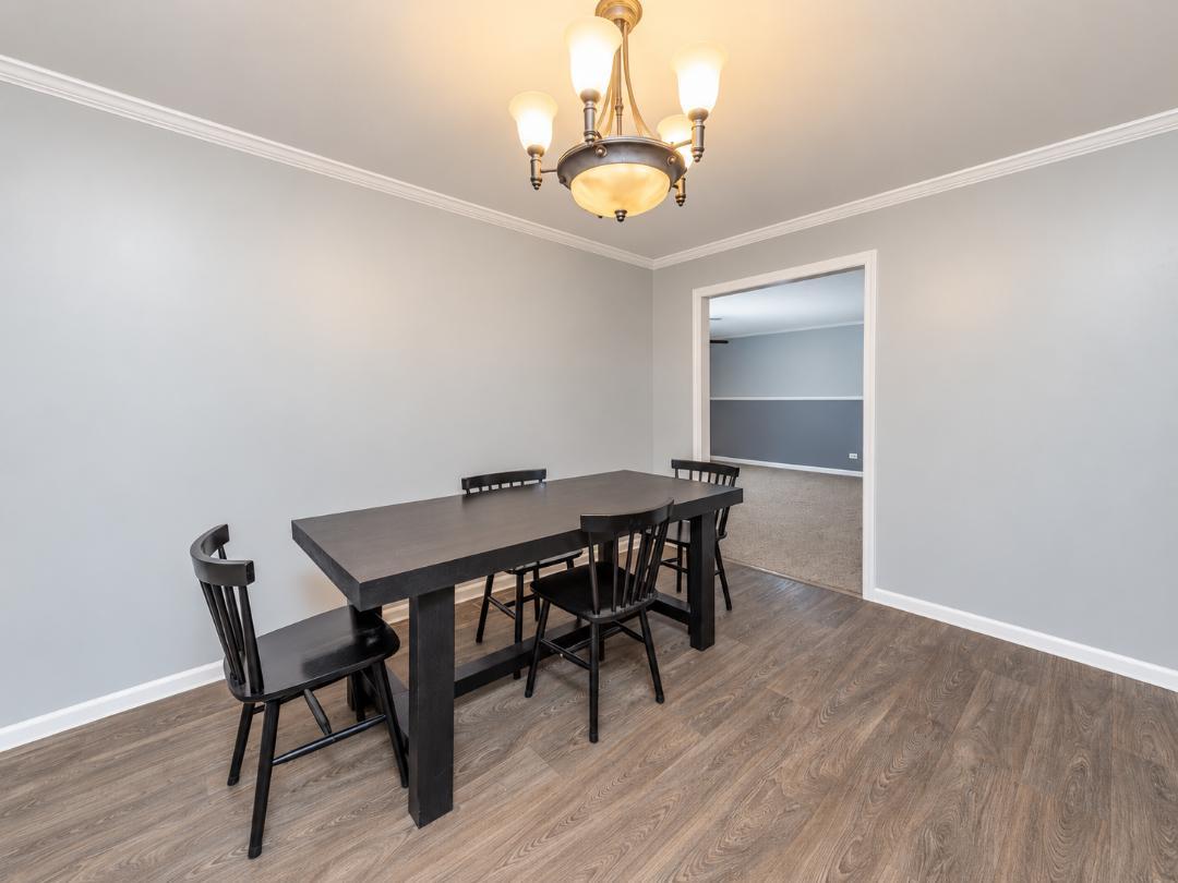 Dining room with a dark table and chairs, wood-look flooring, and a brass chandelier.