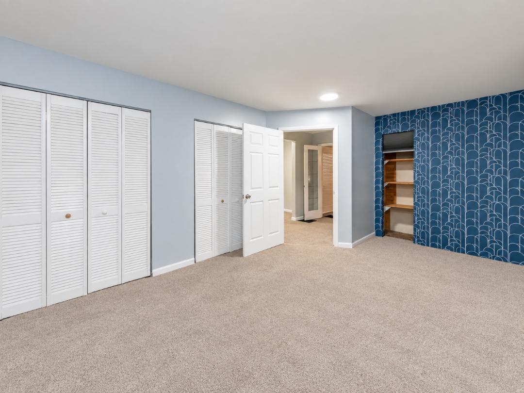 Unfurnished carpeted bedroom with white closets and a blue patterned accent wall.