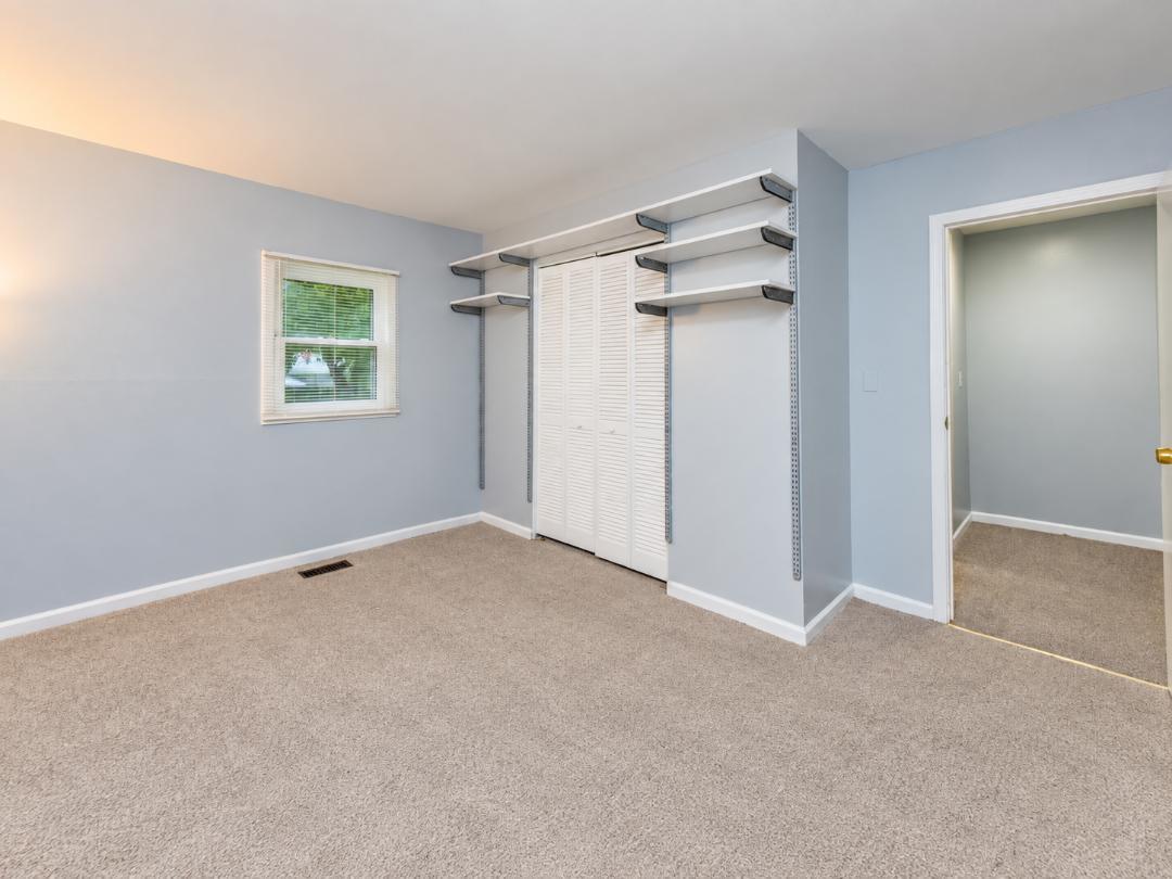 Empty carpeted closet with white louvered doors and wall-mounted shelving.