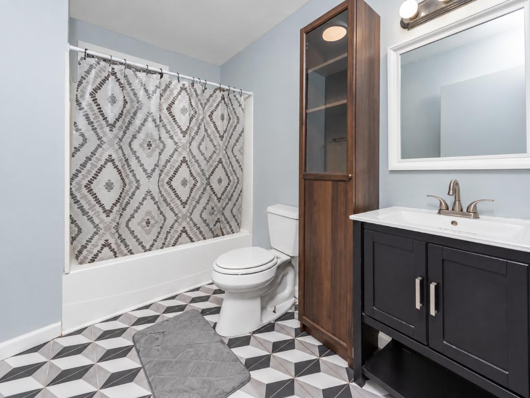 Bathroom with a patterned shower curtain, dark vanity, wood cabinet, and geometric floor tile.