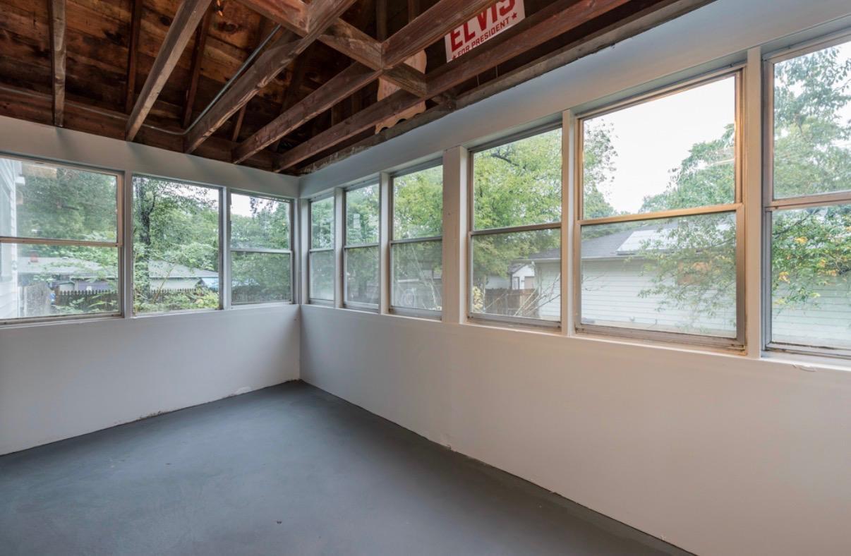 Empty sunroom with large windows on two sides and exposed wooden ceiling beams.