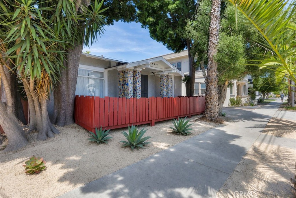Single-story home with a red fence, tiled porch columns, and mature tropical landscaping.