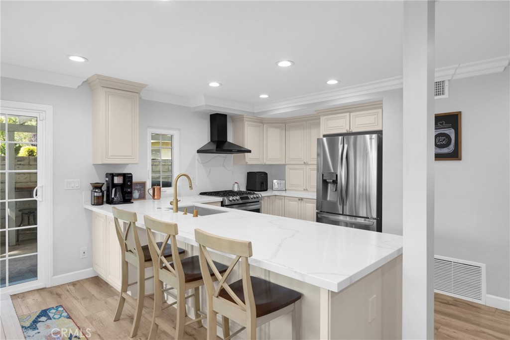 Kitchen with cream cabinetry, stainless steel appliances, and a large island with three bar stools.