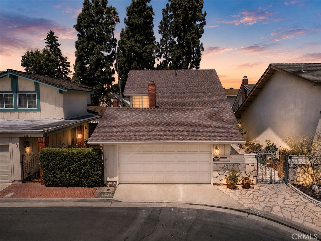 Home exterior with a wide shingle roof, double garage, and stone-paved gated entry at dusk.