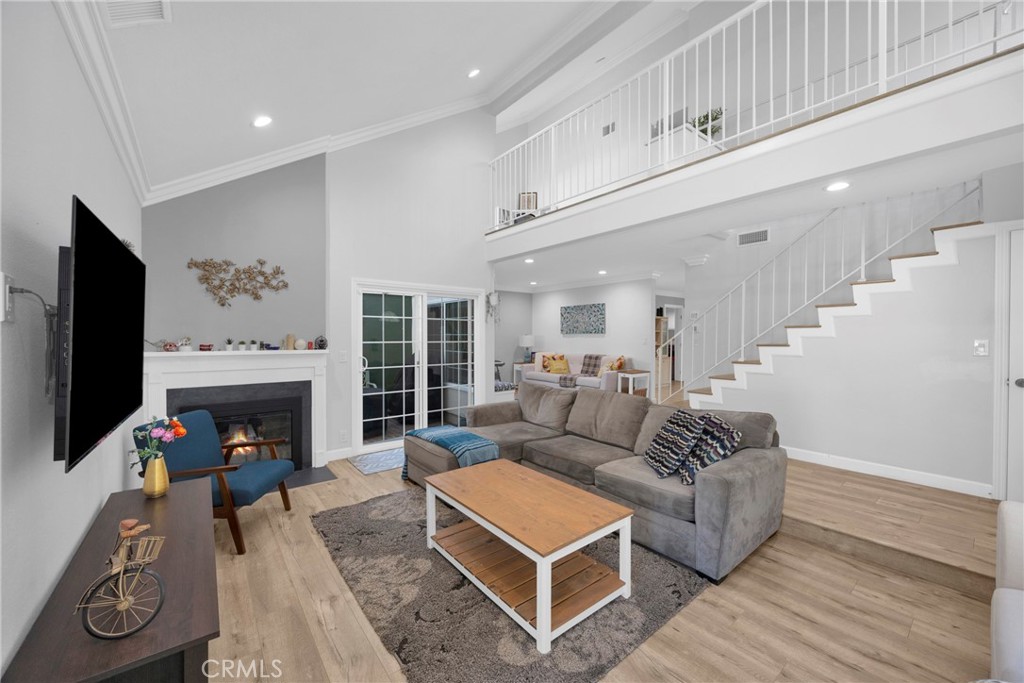 Furnished living room with a fireplace, gray sectional, vaulted ceiling, and open staircase.