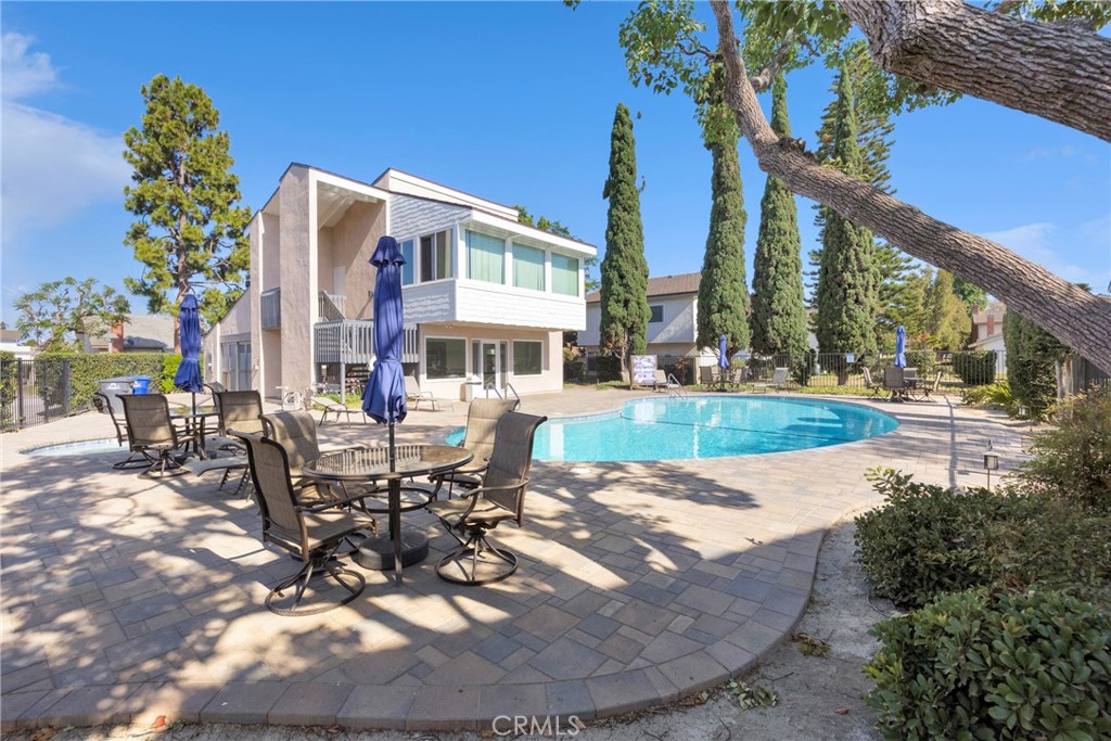 Modern two-story home beside a curved pool and spacious patio with outdoor dining sets.